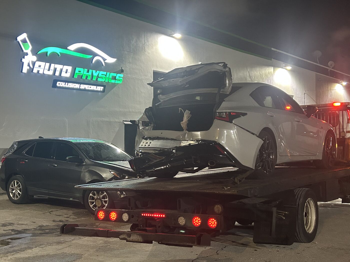 Damaged car arriving on a tow truck at the Auto Physics collision shop
